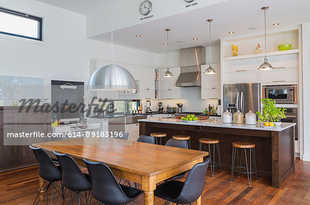 Open plan kitchen dining area with antique table, marble top kitchen island in luxurious modern cube style house interior