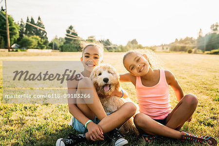 Portrait of smiling happy girls hugging labradoodle puppy in park