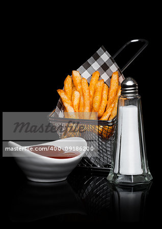 Basket of freshly made southern fries with ketchup and salt black paper on black studio background