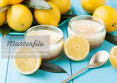 Glass jar with lemon cheesecake with fresh lemons on bluw wooden background