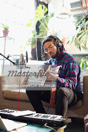 Young man recording music, playing guitar and singing into microphone in apartment