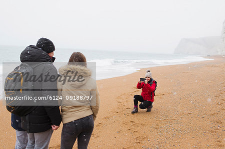 Woman with camera phone photographing husband and daughter on snowy winter beach