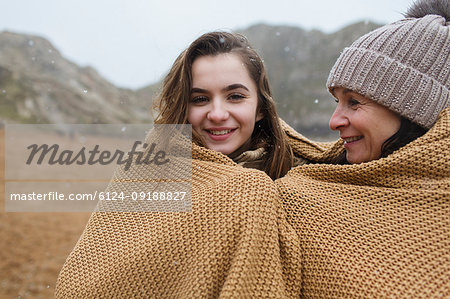 Portrait carefree mother and daughter wrapped in a blanket on snowy winter beach