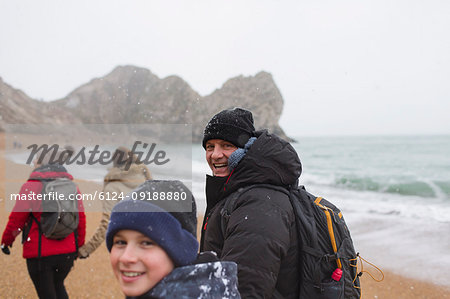 Portrait father and son in warm clothing walking on snowy winter ocean beach