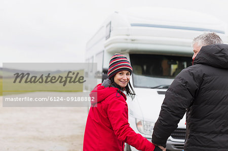 Portrait smiling couple in warm clothing holding hands outside motor home