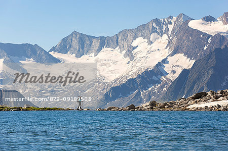 A hiker at Lake Friesenberg with Hoher Weißzint and Hochfeiler on the background, Zillertal Alps, Tyrol, Schwaz district, Austria.