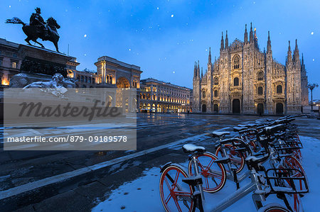 Bicycles parked in PIazza Duomo during snowfall at dusk. Milan, Lombardy, Northern Italy, Italy.