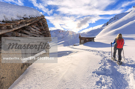 Young girl walks with snowshoes between traditional huts. Grevasalvas, Engadin Valley, Graubünden, Switzerland, Europe.