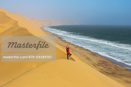 Man take yoga tree pose from the top of the sand dunes,Sandwich Harbour,Namib Naukluft National Park,Namibia,Africa Man take yoga tree pose from the top of the sand dunes,Sandwich Harbour,Namib Naukluft National Park,Namibia,Africa