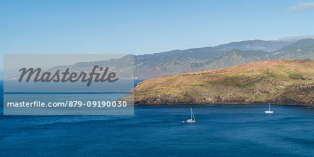 Boat sailing on the Atlantic Ocean at Point of St Lawrence, with the village of Canical in the background. Machico district, Madeira region, Portugal.