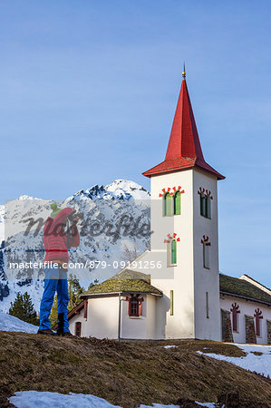 Photographer in action while the church tower frames the snowy peaks Maloja Pass Canton of Graubunden Switzerland