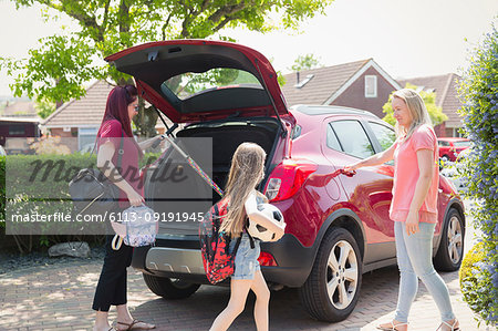 Lesbian couple and daughter loading car for school in sunny driveway