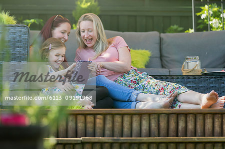Lesbian couple and daughter using digital tablet on patio