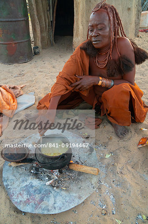 One senior red ochred Himba woman cooking her meal on an open fire, Puros Village, near Sesfontein, Namibia, Africa