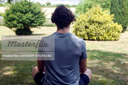 Young man practicing yoga in garden, rear view lotus pose