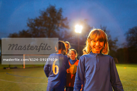 Portrait confident girl playing soccer with team on field at night