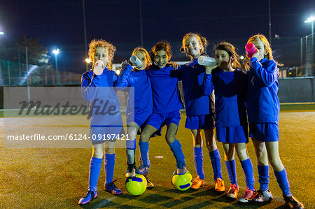 Portrait confident girls soccer team drinking water on field at night