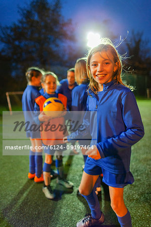 Portrait smiling, confident girl soccer player practicing with team on field at night