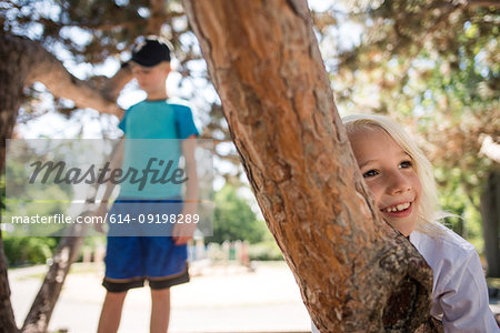 Happy boy leaning against tree branch, sister in background