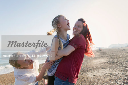 Lesbian couple and daughter laughing on sunny beach