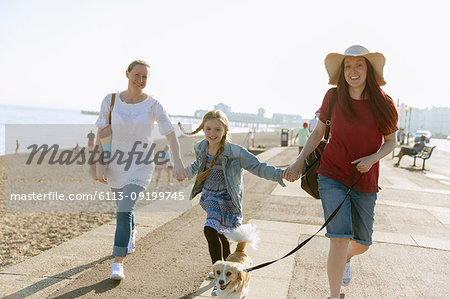 Lesbian couple walking with daughter and dog on sunny beach boardwalk