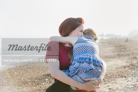 Affectionate mother holding daughter on sunny beach