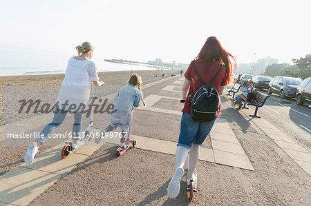 Lesbian couple with daughter riding push scoters on sunny beach boardwalk