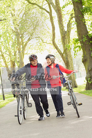 Active senior couple walking bicycles in park