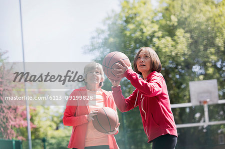 Active senior women friends playing basketball in sunny park
