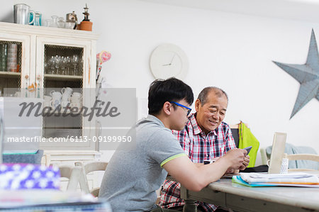 Son helping senior father paying bills at laptop