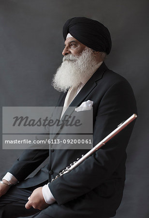 Portrait serious, well-dressed senior man in turban holding flute