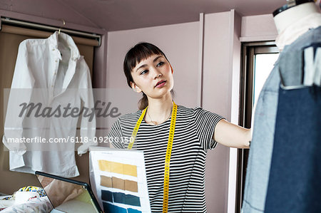 Japanese female fashion designer working in her studio, looking at garment on dressmaker's model.