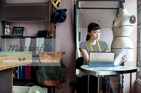 Japanese female fashion designer working in her studio, sitting at table, looking at fabric samples.