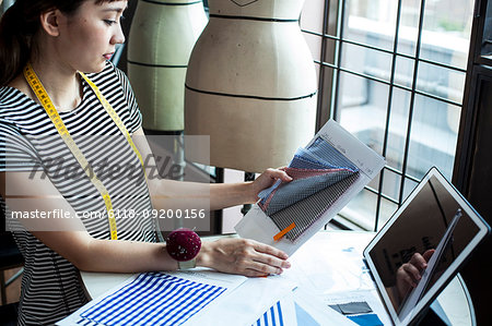Japanese female fashion designer working in her studio, sitting at table, looking at fabric samples.