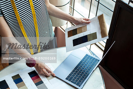 Japanese female fashion designer working in her studio, looking at fabric samples, using laptop.