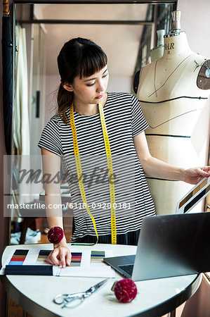 Japanese female fashion designer standing at desk, working in her studio.