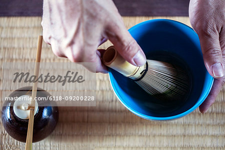 High angle close up of person using bamboo whisk to prepare Matcha tea in a blue bowl during tea ceremony.