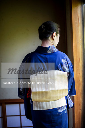 Rear view of Japanese woman wearing traditional bright blue kimono with cream coloured obi.