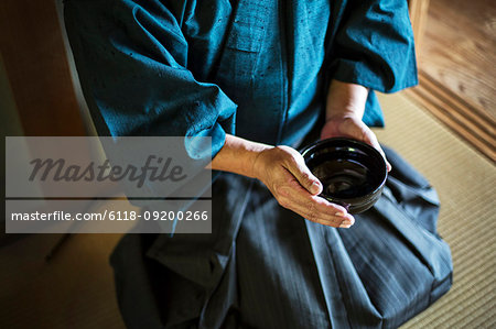 High angle close up of Japanese man wearing kimono holding tea bowl during tea ceremony.