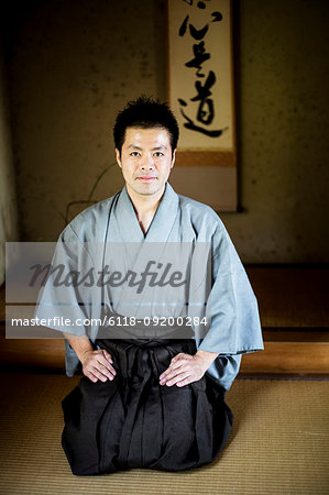 Japanese man wearing kimono sitting on floor in traditional Japanese house, looking at camera.