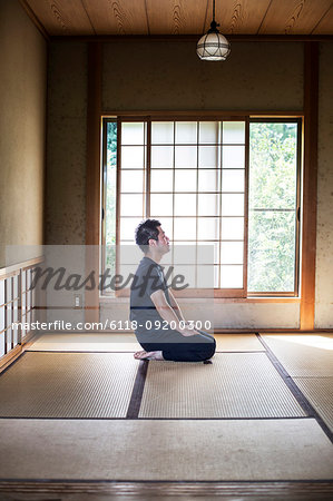 Japanese man kneeling on tatami mat in traditional Japanese house.