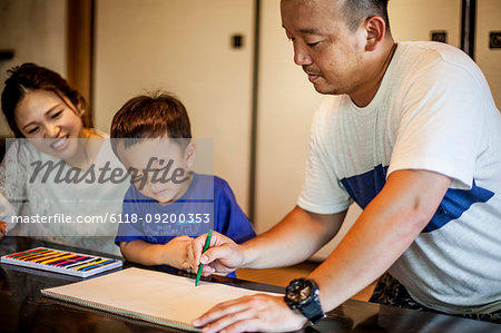 Japanese woman, man and little boy sitting at a table, drawing with colouring pens.