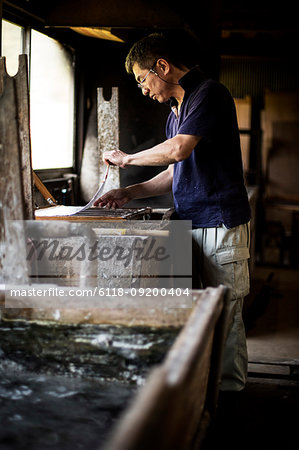 Japanese man in a workshop, holding a wooden frame with pressed pulp, making traditional Washi paper.