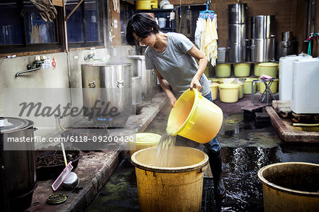 Japanese woman working in a textile plant dye workshop, pouring hot water into yellow plastic buckets.