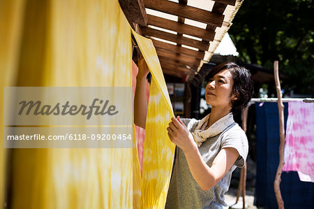 Japanese woman standing in a textile plant dye workshop, hanging up freshly dyed bright yellow fabric.