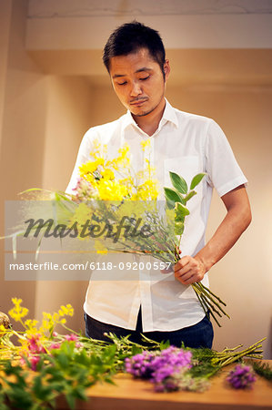 Japanese man in a flower gallery, working on Ikebana arrangement.