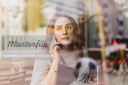 Barista using smart phone behind cafe window