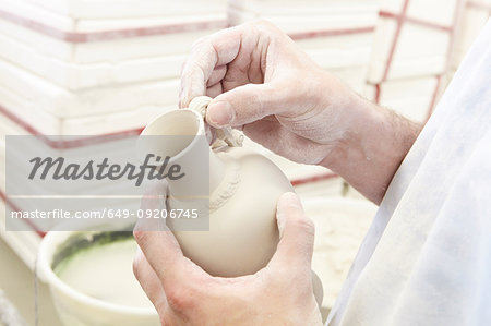 Man attaching handle to jug in pottery factory