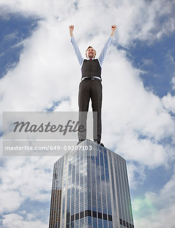 Oversized businessman cheering on skyscraper, low angle view