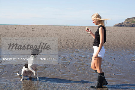 Woman holding ball for dog on beach, Wales, UK
